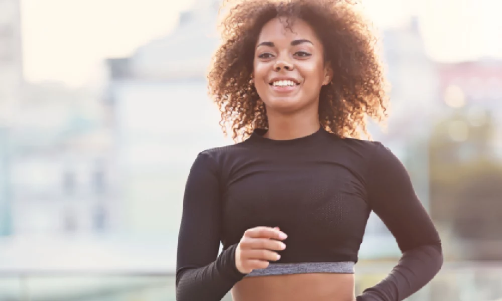 Smiling young woman jogging outdoors, representing active recovery by PRP therapy in San Carlos, CA.